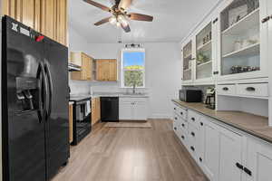 Kitchen with black appliances, glass insert cabinets, light wood finished floors, ceiling fan, and white cabinetry