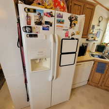 Kitchen with brown cabinetry, white appliances, light countertops, and light flooring
