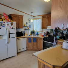 Kitchen featuring white appliances, brown cabinets, light countertops, ornamental molding, and a textured ceiling