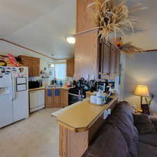 Kitchen featuring white appliances, light countertops, a peninsula, open floor plan, and brown cabinets