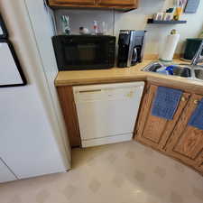 Kitchen featuring brown cabinetry, light countertops, white appliances, open shelves, and light flooring