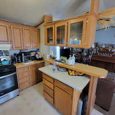 Kitchen featuring stainless steel gas range, brown cabinets, glass insert cabinets, light floors, and a textured ceiling