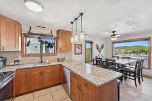 Kitchen with brown cabinetry, light stone countertops, tasteful backsplash, appliances with stainless steel finishes, and a peninsula