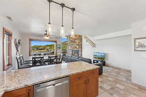 Kitchen featuring brown cabinets, dishwasher, hanging light fixtures, a ceiling fan, and light stone countertops