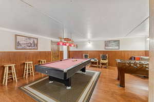 Game room with a textured ceiling, billiards, wainscoting, wood finished floors, and wood walls