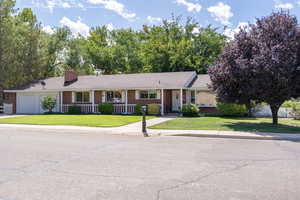 Ranch-style house featuring a front yard, a porch, an attached garage, brick siding, and a chimney