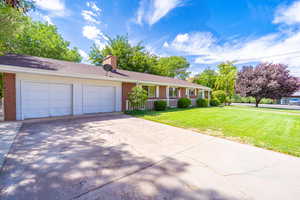Single story home with driveway, brick siding, a front yard, a garage, and a chimney