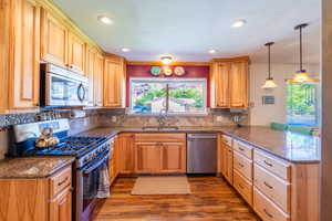 Kitchen featuring appliances with stainless steel finishes, dark stone counters, dark wood-style floors, decorative light fixtures, and recessed lighting