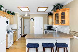Kitchen with backsplash, ornamental molding, a kitchen breakfast bar, a peninsula, and white appliances
