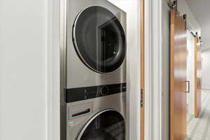Laundry area featuring a barn door and stacked washer / dryer