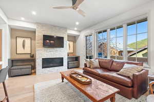 Living area with light wood-style flooring, a stone fireplace, a ceiling fan, and recessed lighting