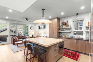 Kitchen featuring a kitchen breakfast bar, open shelves, light wood finished floors, open floor plan, and backsplash
