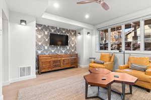Living area featuring an accent wall, wood finished floors, wallpapered walls, and ceiling fan