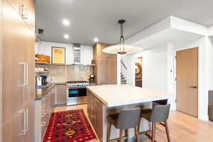 Kitchen with light wood finished floors, modern cabinets, tasteful backsplash, stainless steel range oven, and open shelves