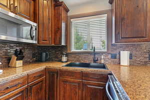 Kitchen featuring stainless steel appliances, tasteful backsplash, and light stone countertops