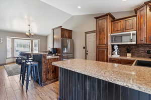 Kitchen featuring a peninsula, a kitchen breakfast bar, lofted ceiling, light stone counters, and appliances with stainless steel finishes