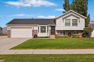 Tri-level home featuring brick siding, a front lawn, an attached garage, and driveway