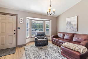 Living room featuring light wood-style floors, a chandelier, and vaulted ceiling