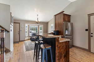 Kitchen featuring a breakfast bar, lofted ceiling, stainless steel refrigerator with ice dispenser, light wood-style flooring, and dark brown cabinets