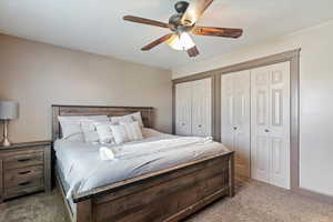 Carpeted bedroom with multiple closets and a ceiling fan