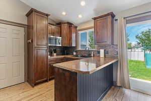 Kitchen featuring light wood-style flooring, stainless steel microwave, decorative backsplash, a peninsula, and recessed lighting