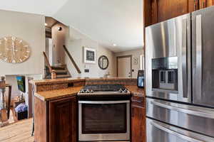 Kitchen featuring stainless steel appliances, dark brown cabinets, a peninsula, light wood-style floors, and dark stone countertops