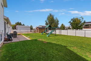 Fenced backyard with a patio, a playground, and a storage unit