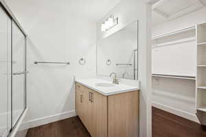 Bathroom with dark wood-style floors, a walk in closet, vanity, and combined bath / shower with glass door