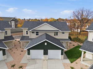 View of front facade featuring stucco siding, roof with shingles, stone siding, concrete driveway, and a garage