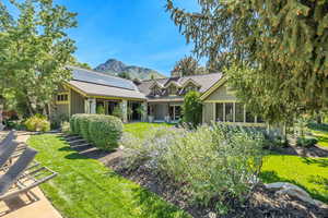 View of back of property with a mountain view, a front lawn, board and batten siding, a chimney, and roof mounted solar panels