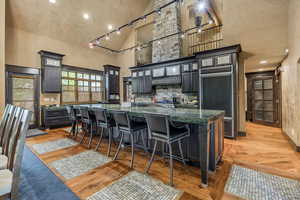 Kitchen featuring high vaulted ceiling, glass insert cabinets, a breakfast bar, a large island with sink, and dark cabinets