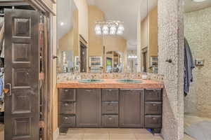 Ensuite bathroom featuring double vanity, light tile patterned floors, and high vaulted ceiling