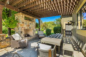 View of patio with outdoor dining space, an outdoor stone fireplace, and a pergola