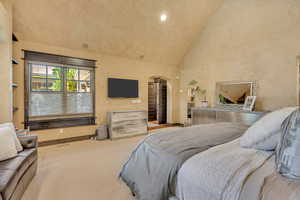 Primary Bedroom featuring high vaulted ceiling, arched walkways, carpet flooring, and recessed lighting
