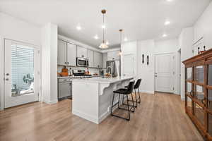 Kitchen featuring gray cabinetry, a kitchen breakfast bar, hanging light fixtures, an island with sink, and stainless steel appliances