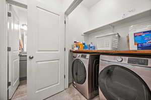 Washroom with washing machine and dryer and light tile patterned flooring