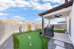 Fenced backyard featuring a ceiling fan, a patio area, and a putting area