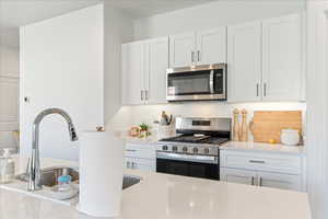Kitchen featuring stainless steel appliances, white cabinetry, and light stone counters