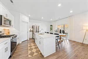 Kitchen with appliances with stainless steel finishes, recessed lighting, white cabinets, an island with sink, and light wood-style flooring