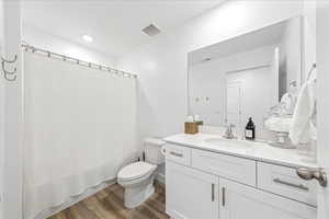 Bathroom featuring dark wood-type flooring, vanity, shower / tub combo with curtain, and recessed lighting