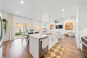 Kitchen featuring white cabinets, appliances with stainless steel finishes, built in shelves, open floor plan, and a center island with sink