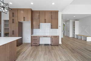 Kitchen with recessed lighting, brown cabinets, light wood-style flooring, backsplash, and light stone counters