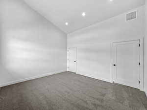 Carpeted empty room with high vaulted ceiling and recessed lighting