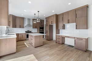 Kitchen with backsplash, hanging light fixtures, wall chimney range hood, a kitchen island, and appliances with stainless steel finishes