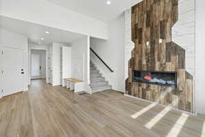 Unfurnished living room featuring a glass covered fireplace, recessed lighting, wood finished floors, and stairs