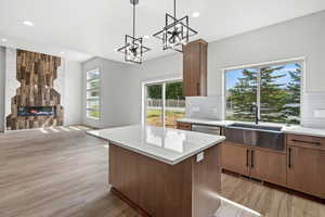 Kitchen with brown cabinetry, tasteful backsplash, open floor plan, pendant lighting, and a tiled fireplace