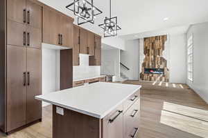 Kitchen featuring light wood-style flooring, a center island, hanging light fixtures, light stone countertops, and a stone fireplace