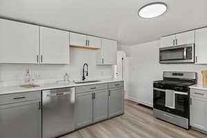 Kitchen featuring gray cabinetry, stainless steel appliances, light wood-type flooring, white cabinetry, and light stone counters
