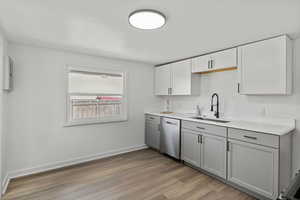 Kitchen featuring gray cabinetry, light wood-type flooring, dishwasher, and white cabinets