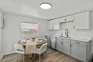 Kitchen featuring light wood-type flooring, gray cabinets, dishwasher, and white cabinetry